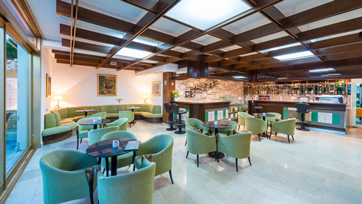 Aperitiv-Bar des Hotels mit Tischen und grünen Samtstühlen